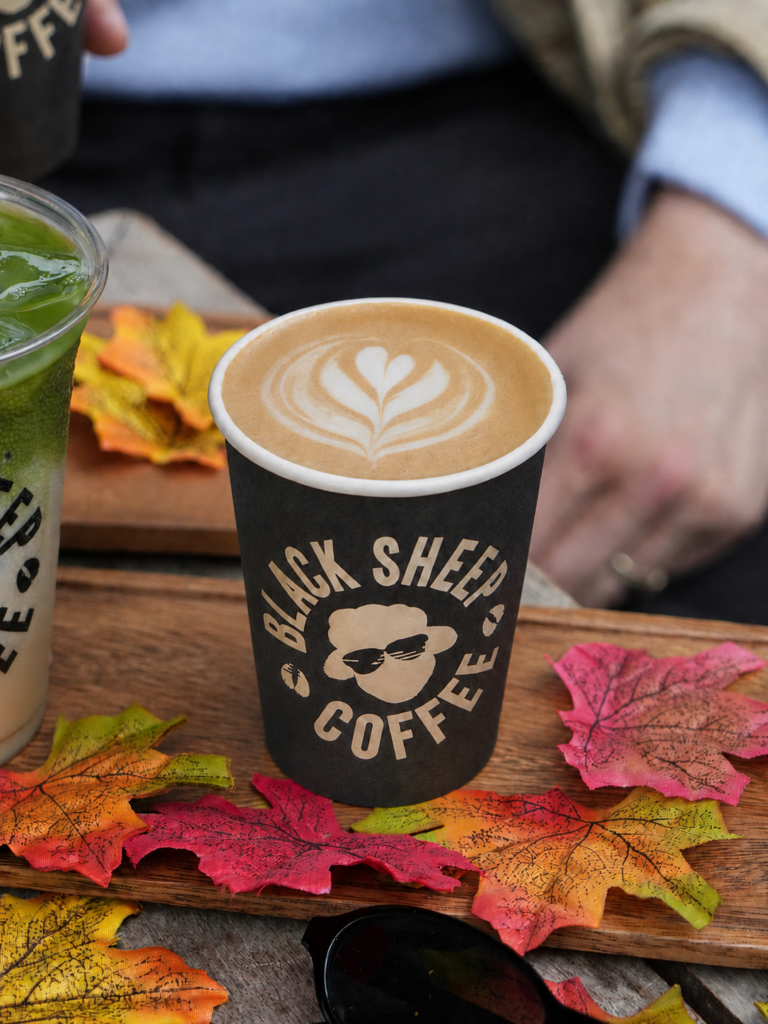 Black Sheep Coffee pumpkin spice latte with heart latte art styled with colourful fall leaves on a wooden tray.